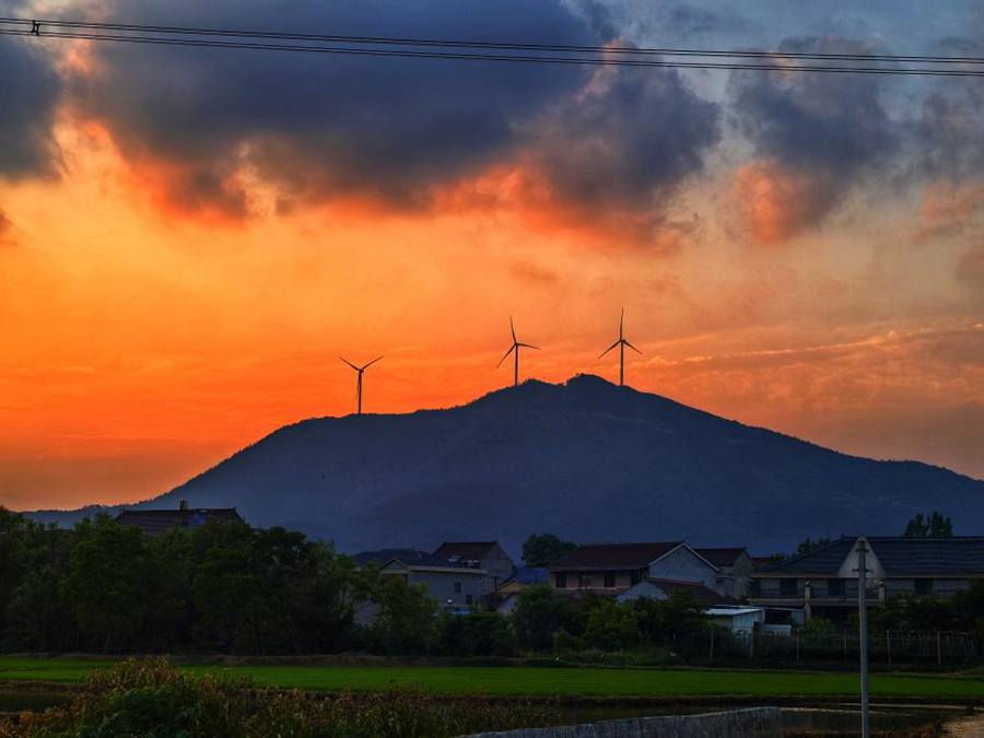 夕阳西沉，将天空晕染得橙红一片，仿佛是大自然用最绚丽的色彩在天地间作画，远处的山峦在这暖色调的映衬下，轮廓分明。（安徽风电太湖风场）